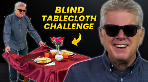 Tommy is holding the edges of a tablecloth for a fully set table